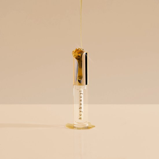 Goudkleurige lipgloss met "hey honey!" op de tube, gouden dop, met druipende honing.
