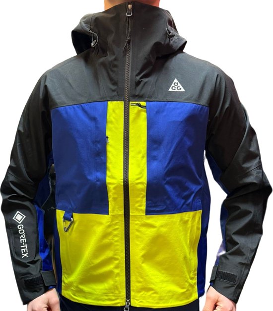Een jas met kleurelementen in geel, blauw en zwart. Het 'GORE-TEX' logo staat op de mouw. Het Nike ACG logo is op de borst.