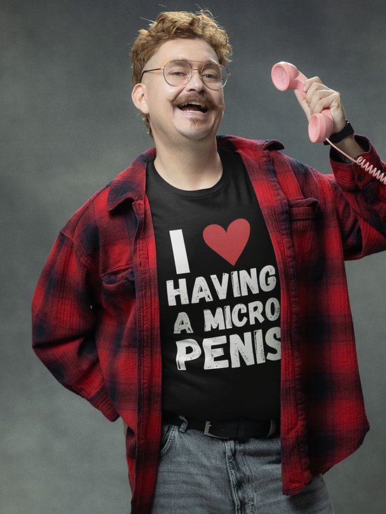Man met bril en snor draagt zwart t-shirt met tekst 'I ❤️ HAVING A MICRO PENIS' en een rood geruite openvallende blouse.