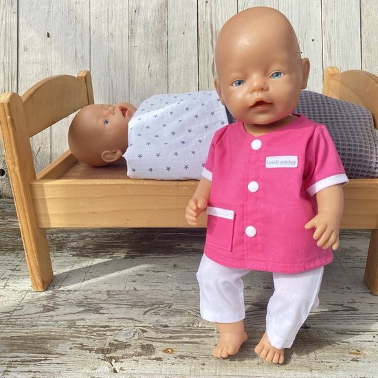 Pop in roze doktersjasje en wit broekje, met een andere pop liggend in een bed op de achtergrond.