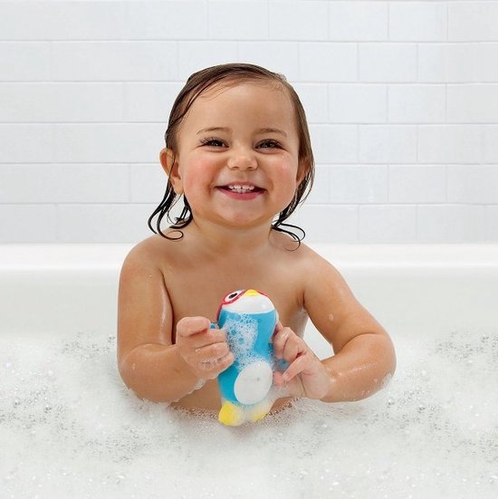 Lachend kind met donkere krullen zit in een bubbelbad en houdt een blauw pinguïn badspeeltje vast.
