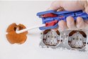 Blauwe kabelstripper met rode inzetstukken, in gebruik bij een muuraansluiting.