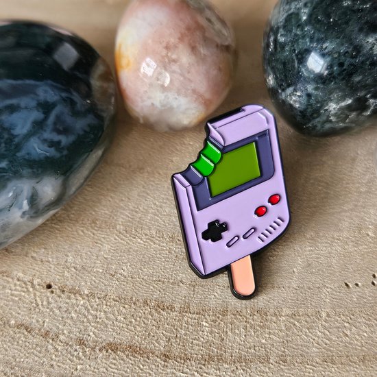 Broche en émail violet en forme de glace Gameboy avec un écran vert et des boutons rouges, avec une morsure.