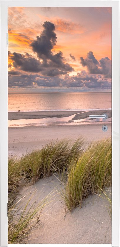 Deursticker met zonsondergang, strand en duingras, op een witte deur.