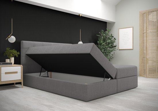 Grijze boxspring met opbergruimte en opengeklapte matras, met een gedetailleerd hoofdbord.