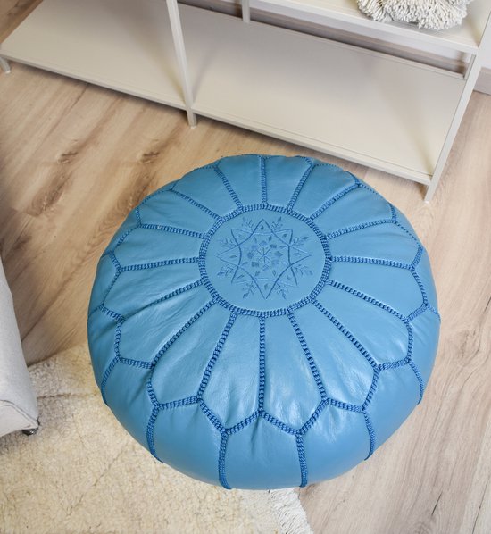 Turkooizen, ronde poef met een stermotief, staand op een houten vloer en een wit vloerkleed.