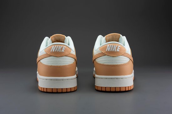 Achterkant van een paar Nike Dunk Low damesschoenen, wit met oranje overlays en 'NIKE' op de hiel.