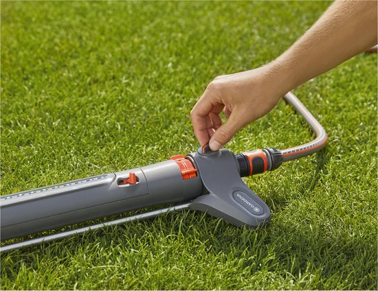Hand draait aan de knop van een Gardena zwenksproeier op een groen gazon.