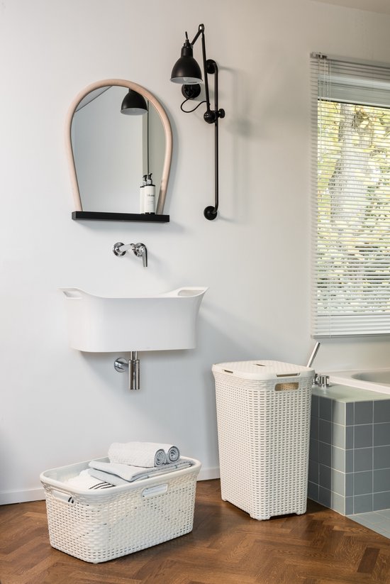 Badkamer met witte wasmanden en een witte wasmand met handvatten, gevuld met handdoeken. Rechts een badkuip.