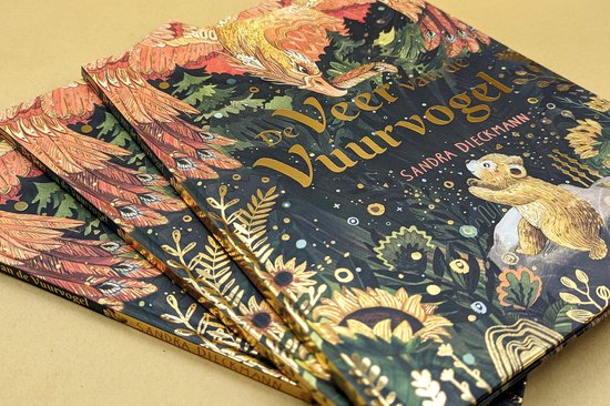 Gestapelde boeken met de titel 'De Veer van de Vuurvogel', met een gouden vuurvogel en een kleine beer op de omslag.