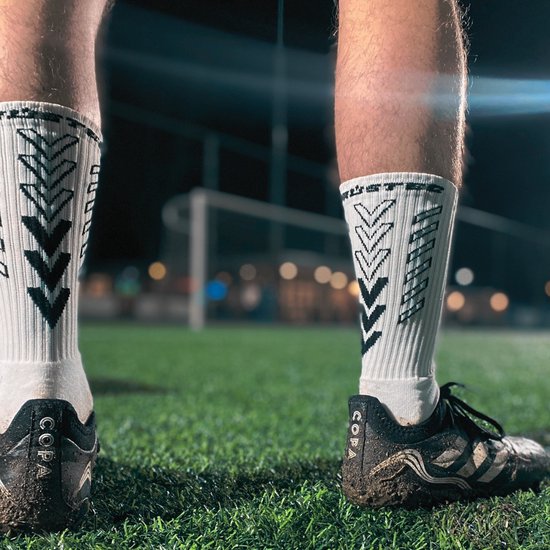 Vue au niveau des chevilles d'un footballeur portant des chaussettes blanches avec des motifs en flèche noirs.