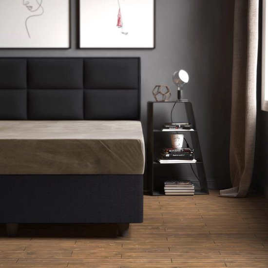 Een zandkleurig hoeslaken op een bed met een zwart hoofdbord.