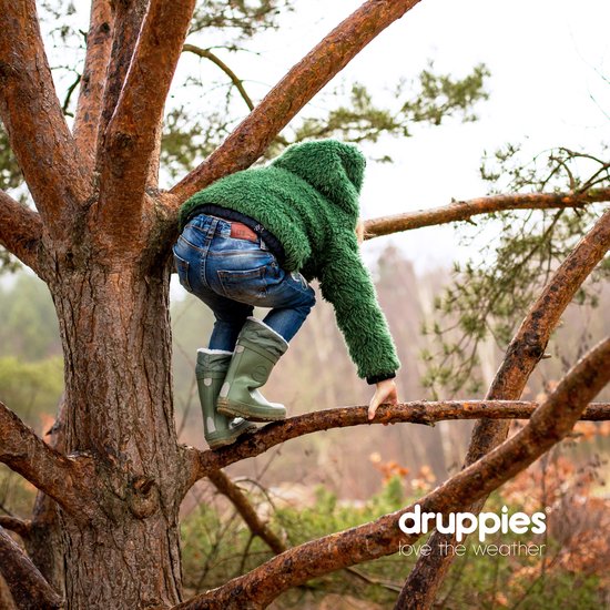 Kind in groene jas en jeans, klimmend in een boom. Draagt groene laarzen.
