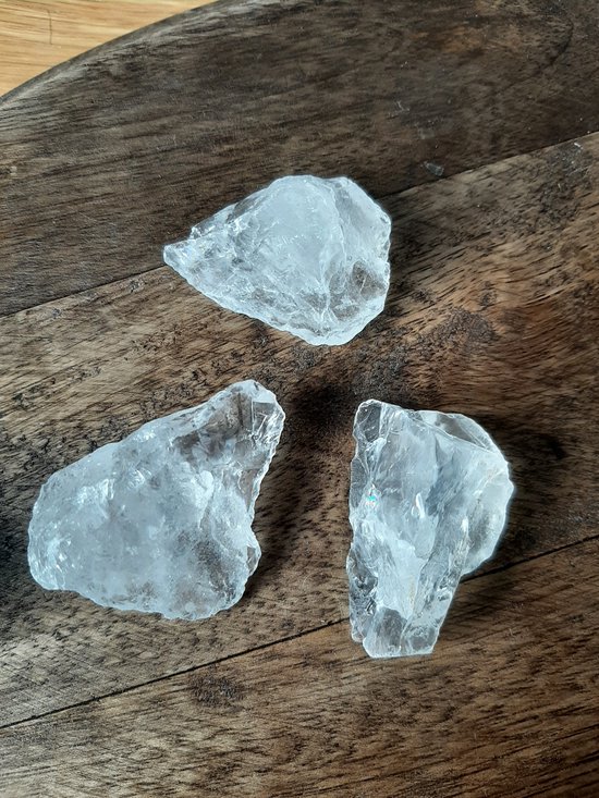 Drie ruwe, heldere bergkristallen op een houten ondergrond.