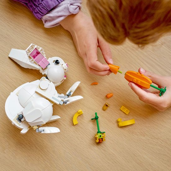 Des mains d'enfants construisent un lapin LEGO blanc.