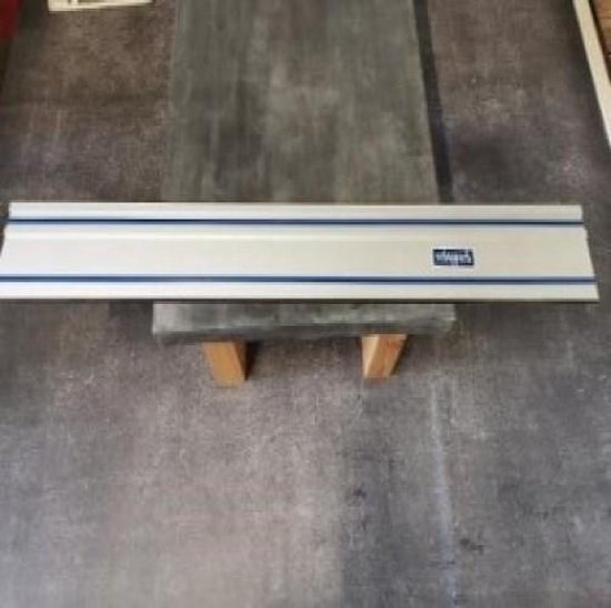Scheppach geleiderail met blauwe strepen, rustend op houten blokken.