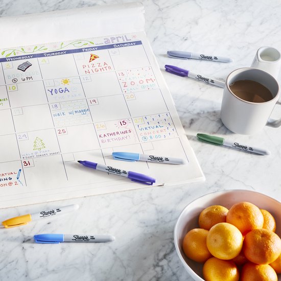 Verschillende Sharpie pennen met fijne punt liggen bij een kalender en een schaal met sinaasappels.