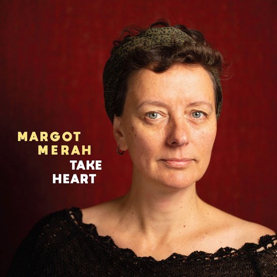 MARGOT MERAH TAKE HEART tekst op rode achtergrond, vrouw in zwart geborduurd topje en hoofdband.