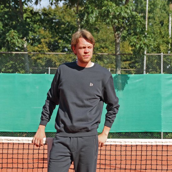 Man op een tennisbaan draagt een donkerblauwe Donnay trui met ronde hals.