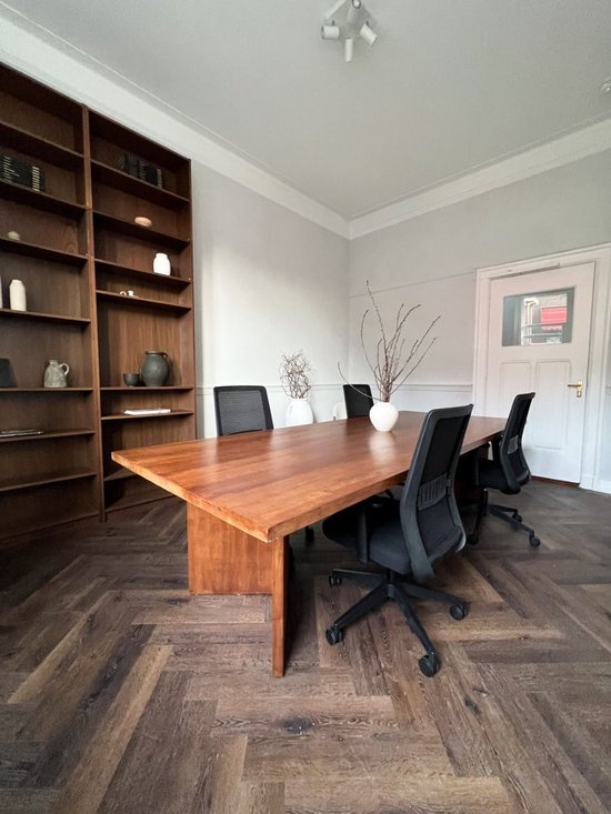 Moderne kantoorruimte met een houten vergadertafel, drie zwarte bureaustoelen en een grote houten boekenkast.