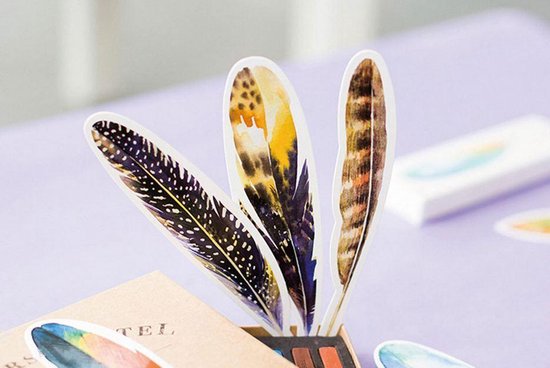 Hand houdt drie papieren verenboekenleggers vast met patronen: zwart met witte spikkels, geelbruin, bruin met zwarte strepen.
