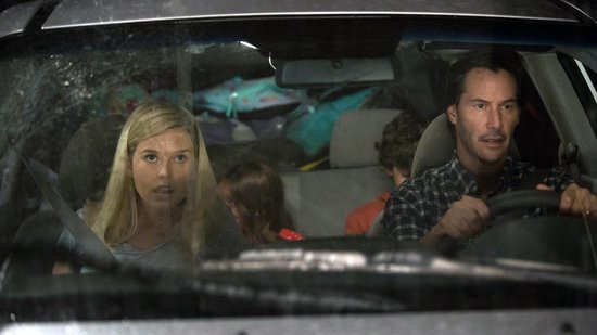 Keanu Reeves rijdt in een auto met drie passagiers, een vrouw en twee kinderen.