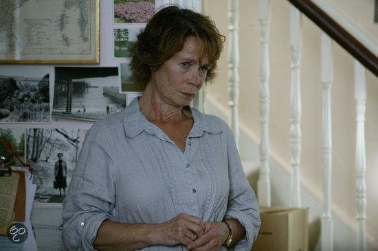 Vrouw met bruin haar, grijze blouse en horloge.