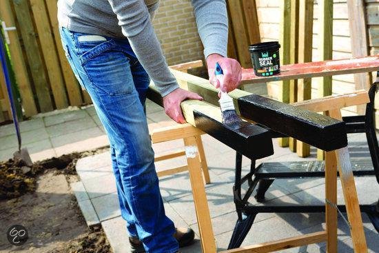 Man met blauwe jeans schildert met zwarte rubbercoating houten balken met een kwast.