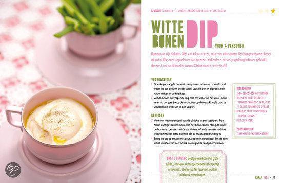 Witte bonendip in een roze schaal, gegarneerd met olie en peper, met op de achtergrond een kopje met groene stengels. Met recept.