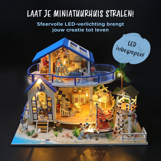 Miniatuur strandhuis met blauw dak, verlichte kamers en balkon. Buiten staat een boot en strandwachttoren. LED verlichting inbegrepen.