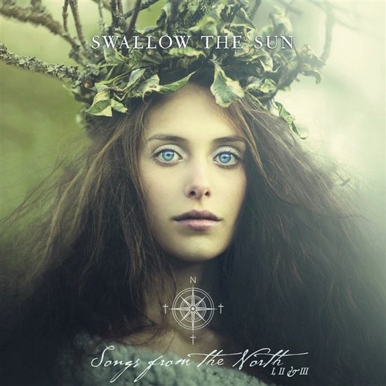 Gros plan d'une femme aux longs cheveux bruns et aux yeux bleu vif, portant une couronne de branches et de feuilles. Texte : SWALLOW THE SUN, Songs from the North I, II & III.