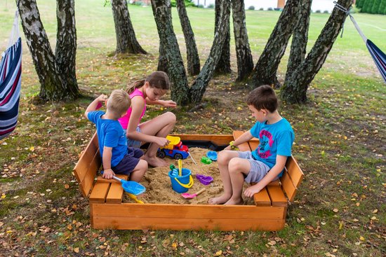 Drie kinderen spelen in een houten zandbak met banken in een tuin.