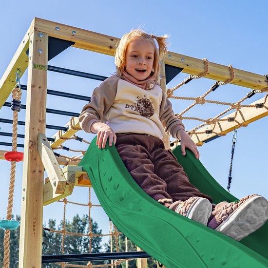 Meisje met staartjes glijdt van een groene glijbaan op een houten klimtoestel.