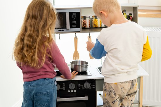 Kinderen spelen met een houten speelkeuken. Jongen pakt pot, meisje houdt pan vast.