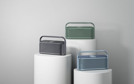 Drie Soundcore Motion X600 speakers in verschillende kleuren: zwart, groen en blauw. De speakers staan op witte displaypilaren.