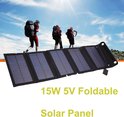 Een uitgevouwen zwart 15W 5V USB zonnepaneel met vijf rijen zonnecellen, op een achtergrond met wandelaars.