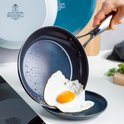 Blauwe koekenpan met antiaanbaklaag, met een spiegelei uit de pan op een bord. Bevat waterdruppels.