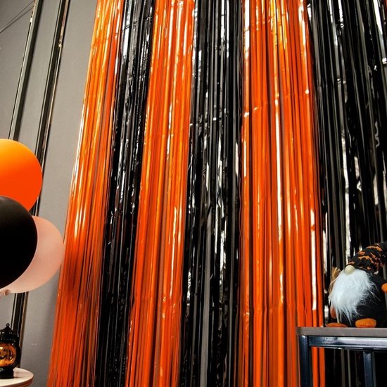 Oranje en zwarte glitterschermen op een feestelijke Halloween-tafel, met ballonnen en een decoratieve pompoen.