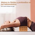 Femme allongée sur un tapis de yoga avec un bloc de liège marron sous le dos, le bloc montrant des illustrations de poses de yoga.