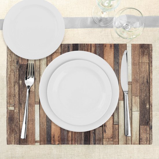 Mise en place de table avec set de table à imprimé planches de bois, assiettes blanches, couverts et verres à vin.