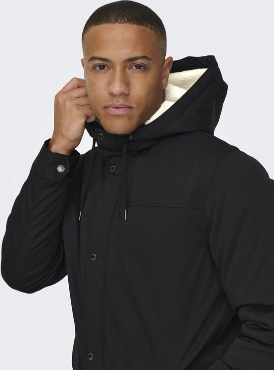 Zijaanzicht van man die de capuchon van een zwarte parka met witte voering vasthoudt.