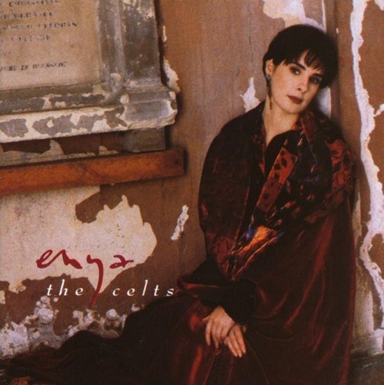 Enya 'The Celts' albumhoes met Enya in een donkerrode jurk, leunend tegen een stenen muur.