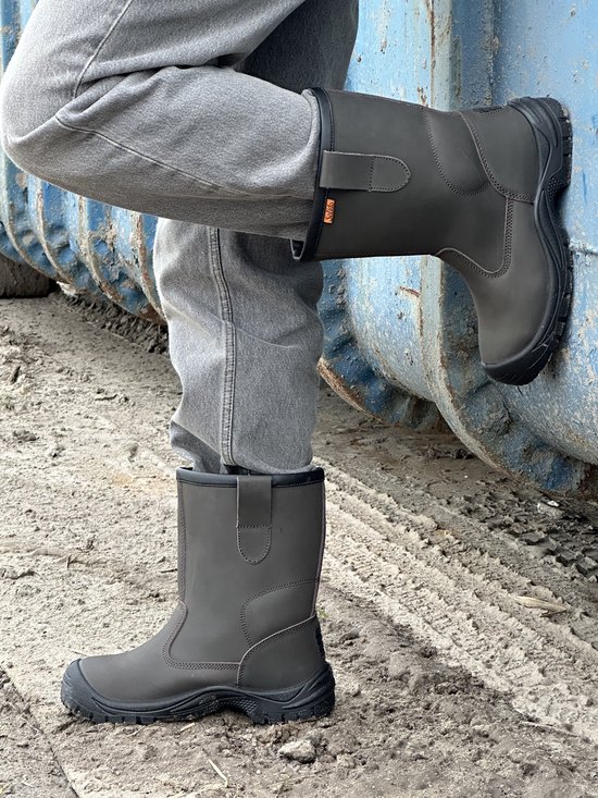 Donkergrijze leren werkschoenen met oranje logo op de zijkant, gedragen met grijze jeans.