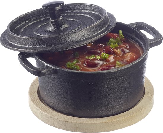 Zwarte gietijzeren braadpan met deksel, gevuld met rode bonenstoofpot en bieslook, op een houten onderzetter.