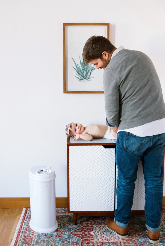 Een vader die een baby verschoont bij een commode, met een witte Ubbi luieremmer ernaast.