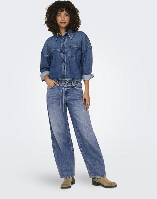 Model in een blauwe denim spijkerbroek met wijde pijpen en ceintuur, gedragen met een blauwe denim blouse.