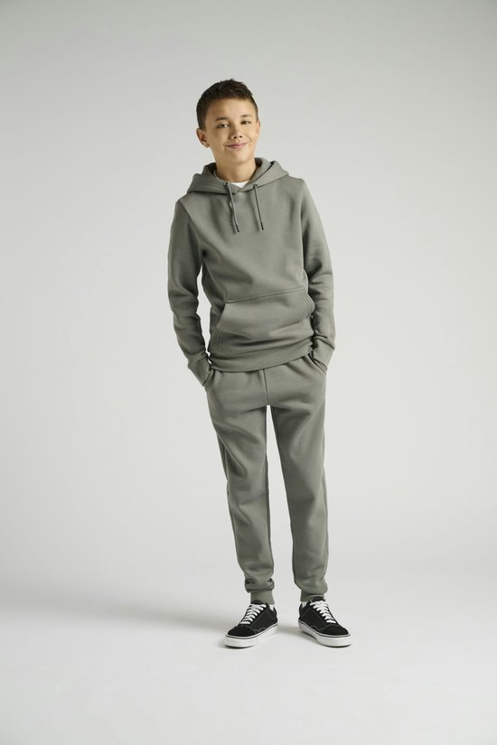 Jongen met handen in de zakken van een olijfgroene joggingbroek, met een bijpassende capuchon.