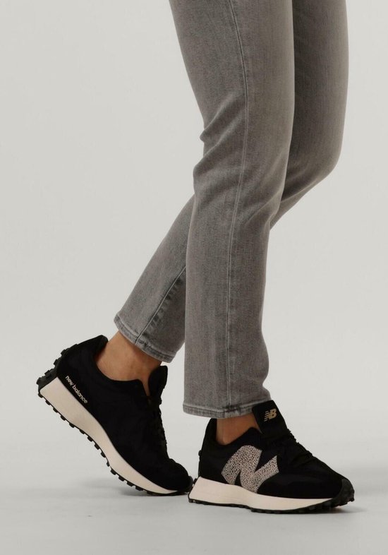 Een persoon draagt zwarte New Balance 327 sneakers met beige luipaardprint N-logo, met grijze jeans.