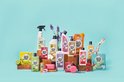 Collectie Marcel's Green Soap producten, waaronder spuitflessen, navulflessen en zepen, met fruit en bloemen op een lichtblauwe achtergrond.