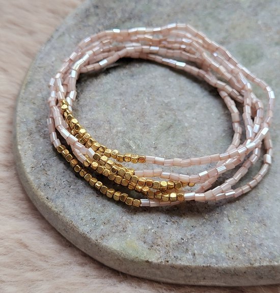 Drie armbandjes met lichtroze parelmoeren en goudkleurige kralen op een steen.